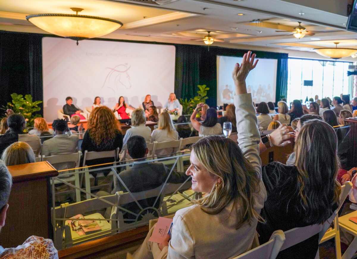 Conferance attendees, one woman with hand raised