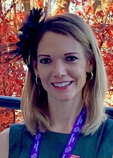 Woman with blue shirt and lanyard with flower in hair and autumn leaves in back