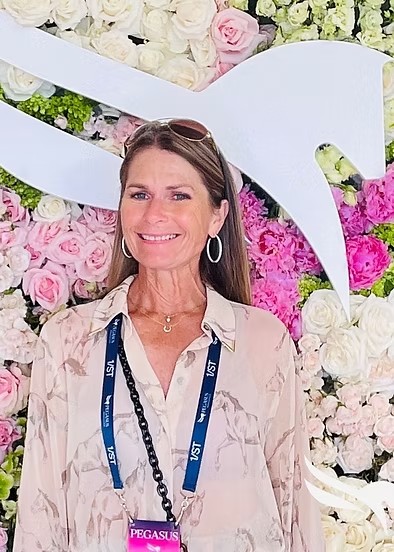 Woman in white shirt with horse pattern in front of wall of flowers
