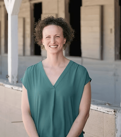 Woman wearing green blouse standing outside a row of stalls