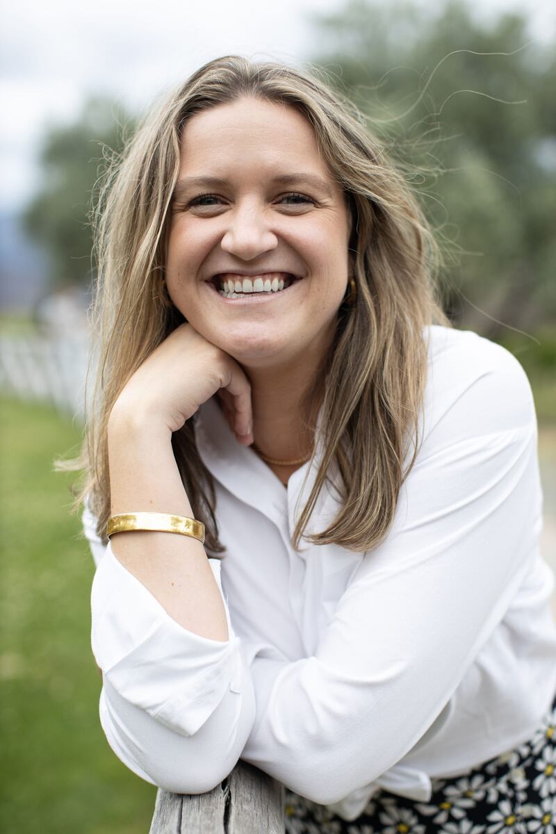 Shannon Kelly, wearing white shirt and dark flowered skirt, leaning on fence